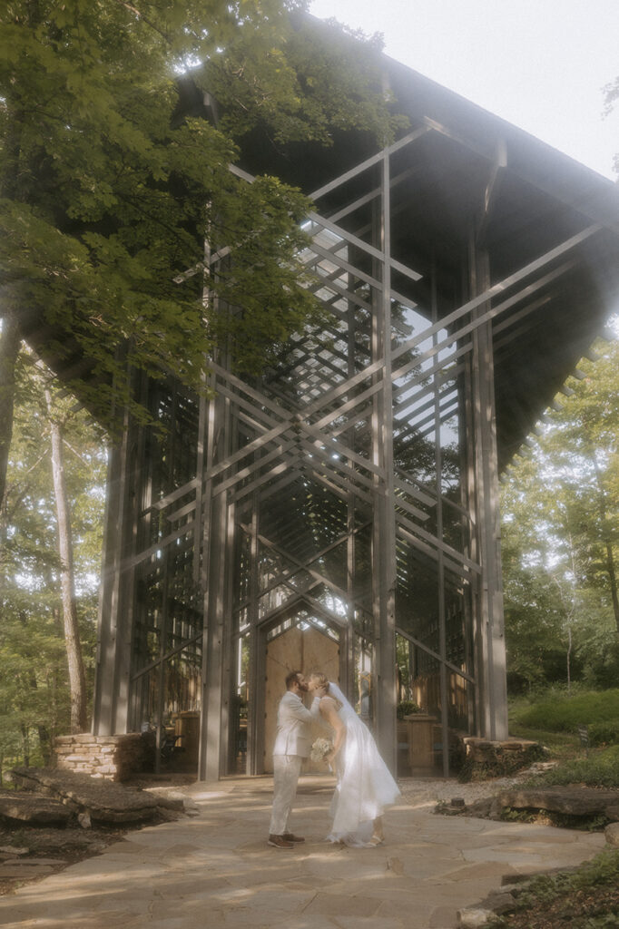 A couple in wedding attire go in for a kiss outside of Thorncrown Chapel in Eureka Springs after just eloping inside.