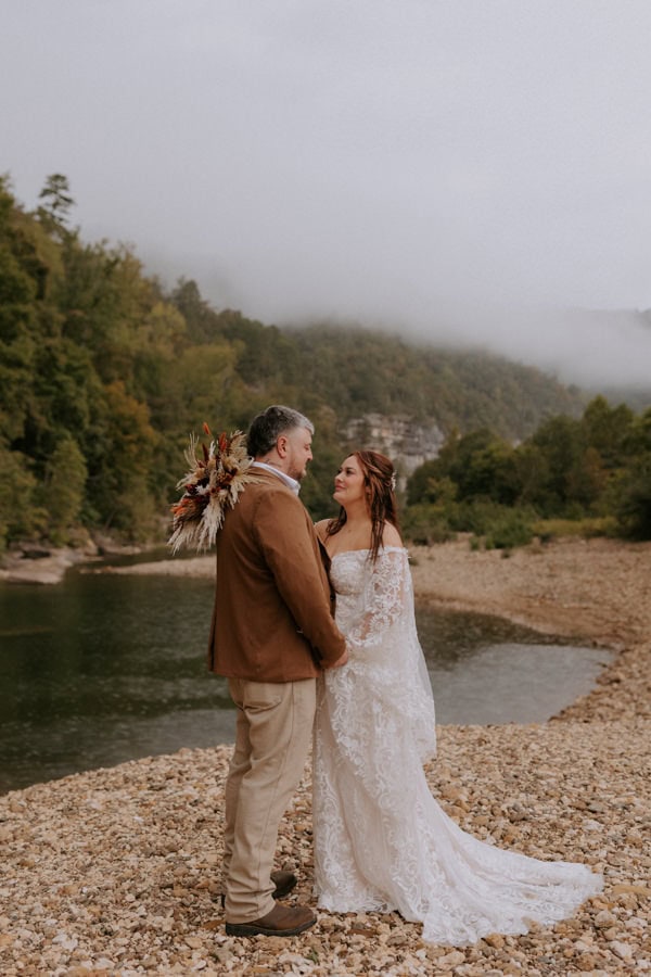 A couple embraces in the rain in front of the Buffalo National River during their Arkansas elopement in Ponca.