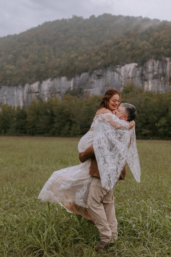 A groom picks up his bride and spings her around while they play in the rain at Steel Creek Campground during their Buffalo National River Arkansas elopement.