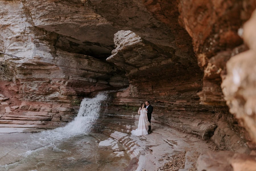 A bride and groom embrace next to a waterfall during their Arkansas elopement at Lost Valley Trail in Ponca.