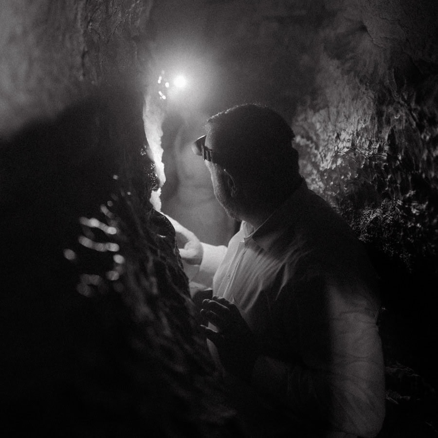 A groom squeezes through a narrow space while caving during an adventure elopement in Ponca, Arkansas.