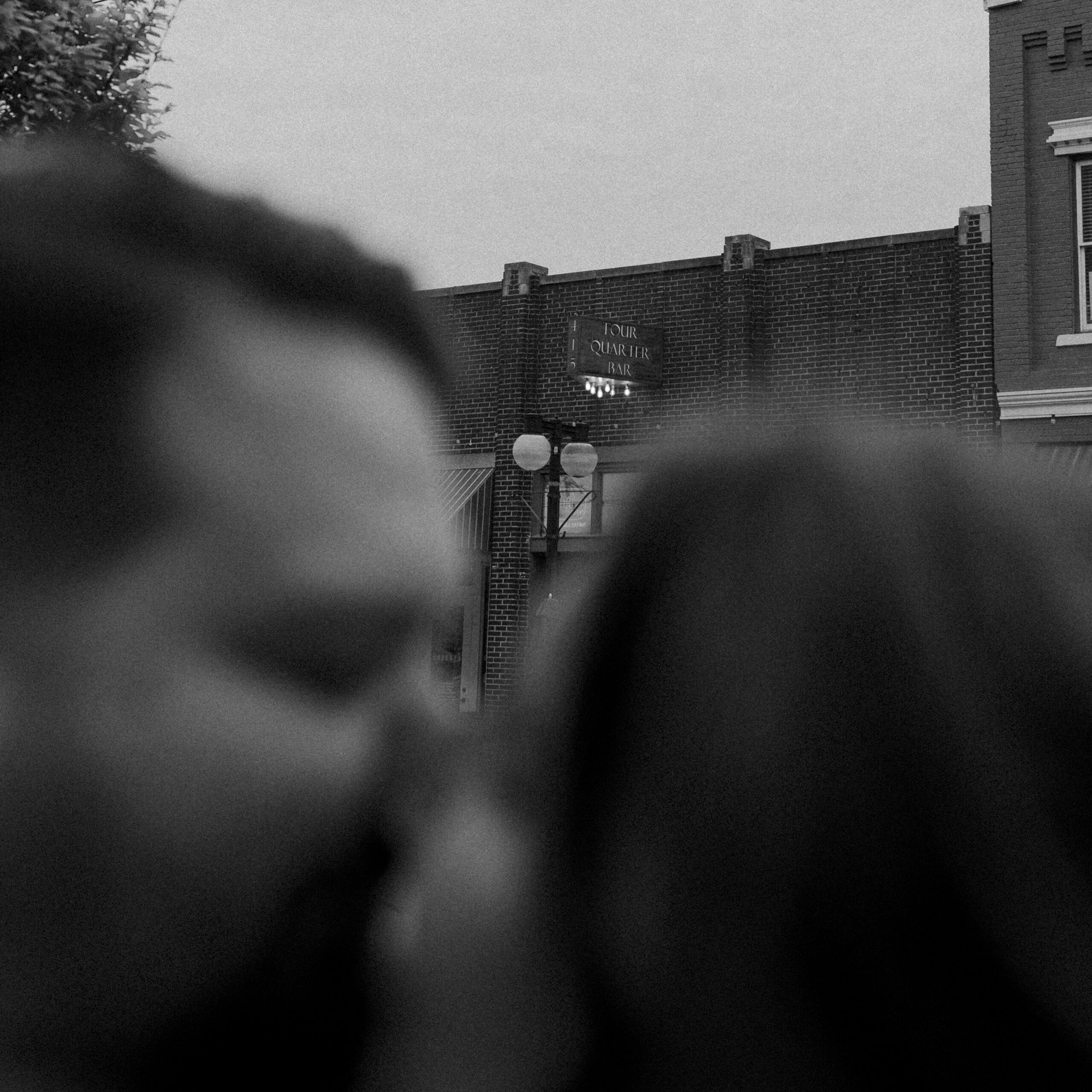 A couple kissing in the foreground up close to the camera. The focus is on Four Quarter Bar's sign in the background, a restaurant in North Little Rock's Argenta District.