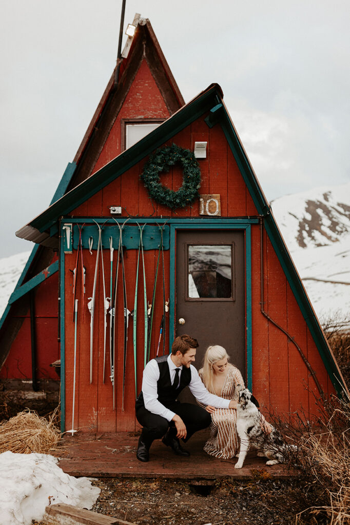 A couple lean down to pet their dog during their snowy elopement at Hatcher Pass in Alaska.