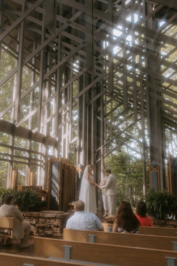 A bride and groom hold hands at the altar during their ceremony at Thorncrown Chapel while eloping in Eureka Springs, Arkansas.