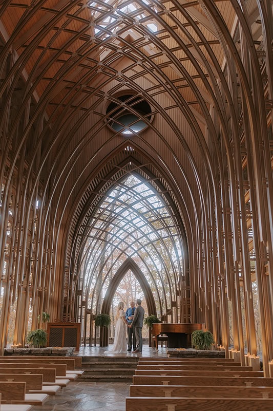 A bride and groom stand at the altar inside of a glass chapel during their Arkansas elopement at Cooper Chapel in Bella Vista.