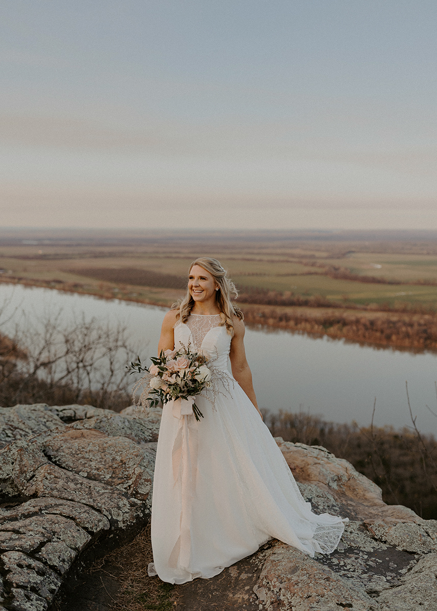 A bride laughs while standing on a cliffside at Petit Jean State Park during her vow renewal in Arkansas.