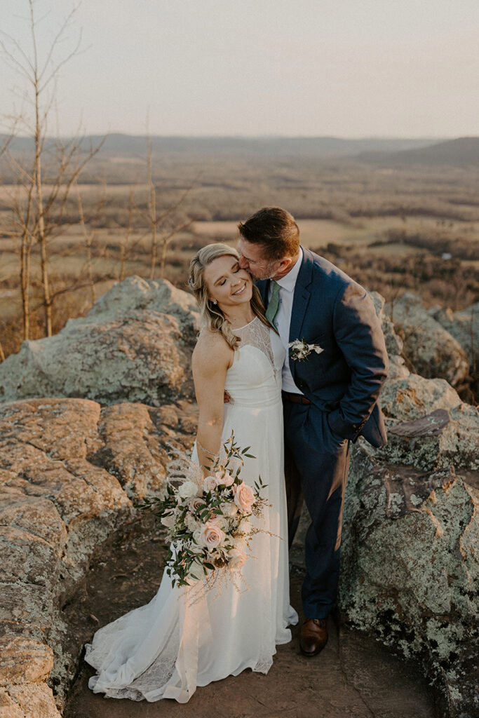 A groom embraces and kisses his bride on the cheek for a photo at Petit Jean State Park during their Arkansas elopement.