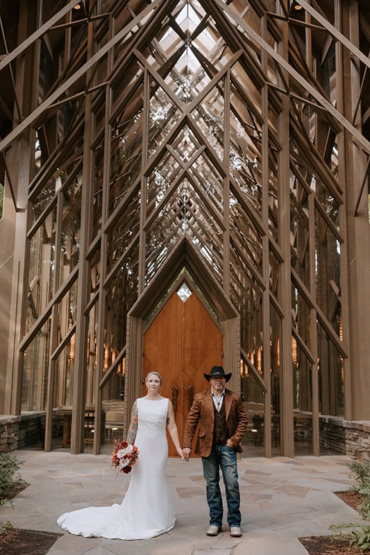 A couple stands in front of the doors of Anthony Chapel, a glass chapel in Hot Springs, Arkansas, posing for their wedding photos.