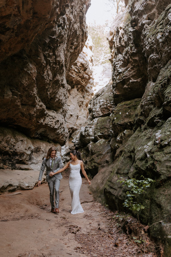 a couple holds hands and walks through the cave formations at Bear Cave Trail during their Arkansas elopement at Petit Jean State Park.