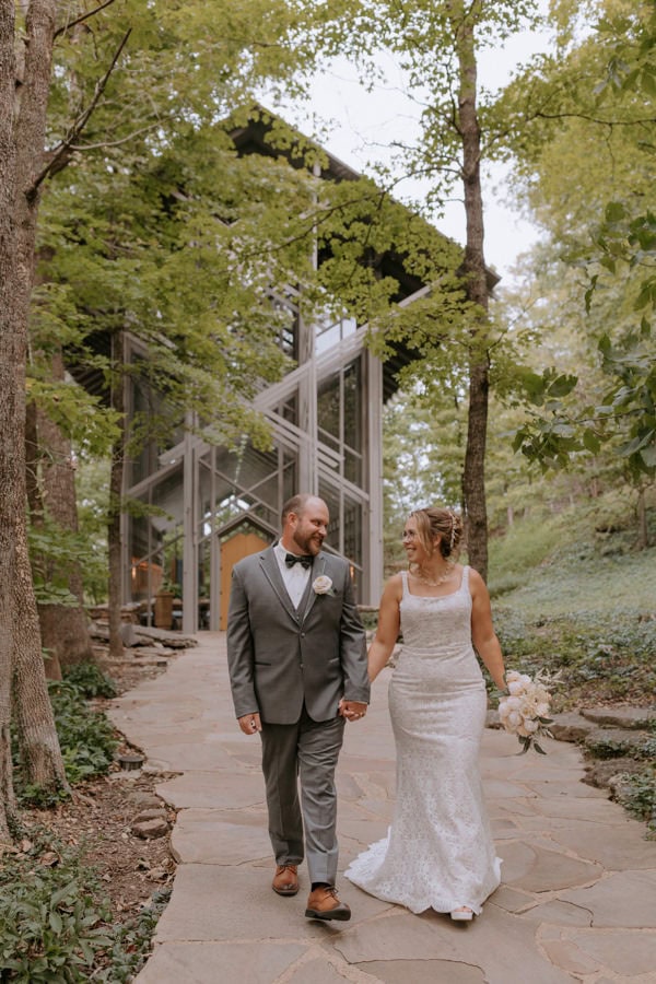 A bride and groom hold hands smiling and walking away from Thorncrown Chapel in Eureka Springs after just eloping in Arkansas.