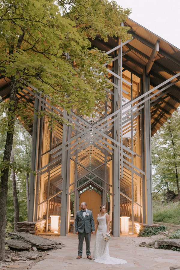 A bride and groom pose for a photo outside of a lit up Thorncrown Chapel during their evening elopement in Eureka Springs, Arkansas.