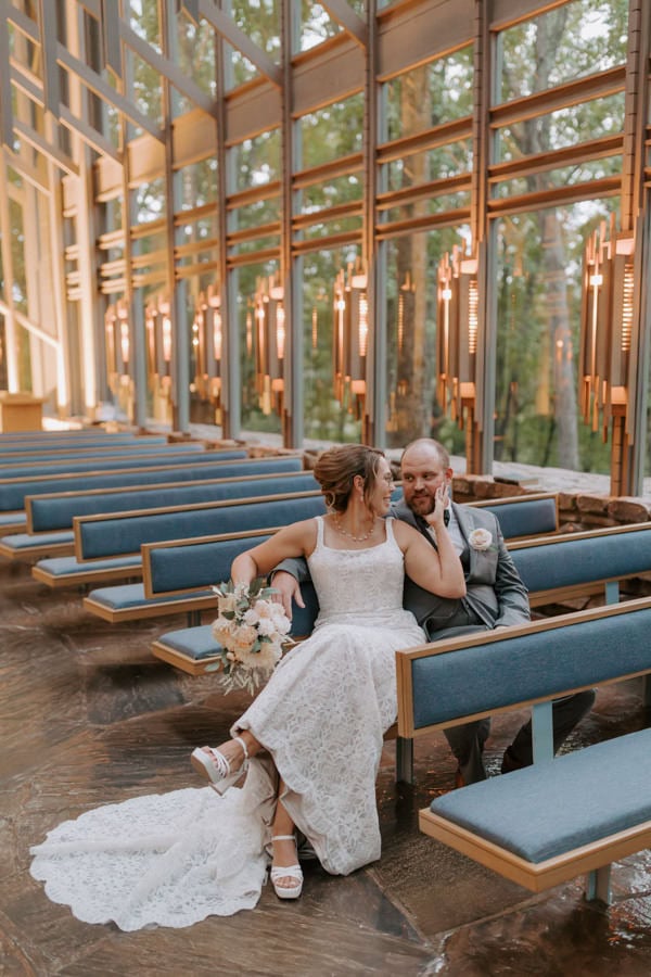 A bride and groom sit next to each other in the pews of Thorncrown Chapel posing for a photo during their elopement in Arkansas.
