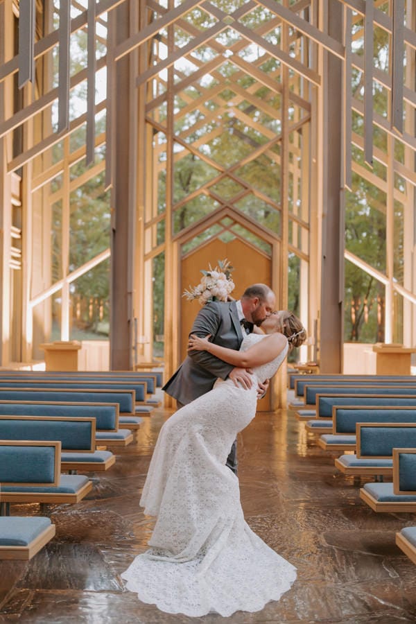 A couple leans down for a dip kiss inside of a glass chapel during their Arkansas elopement photos at Thorncrown Chapel in Eureka Springs, Arkansas.