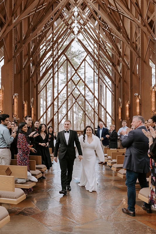 A bride and groom walk down the aisle smiling after just getting married at Anthony Chapel at Garvan Gardens.