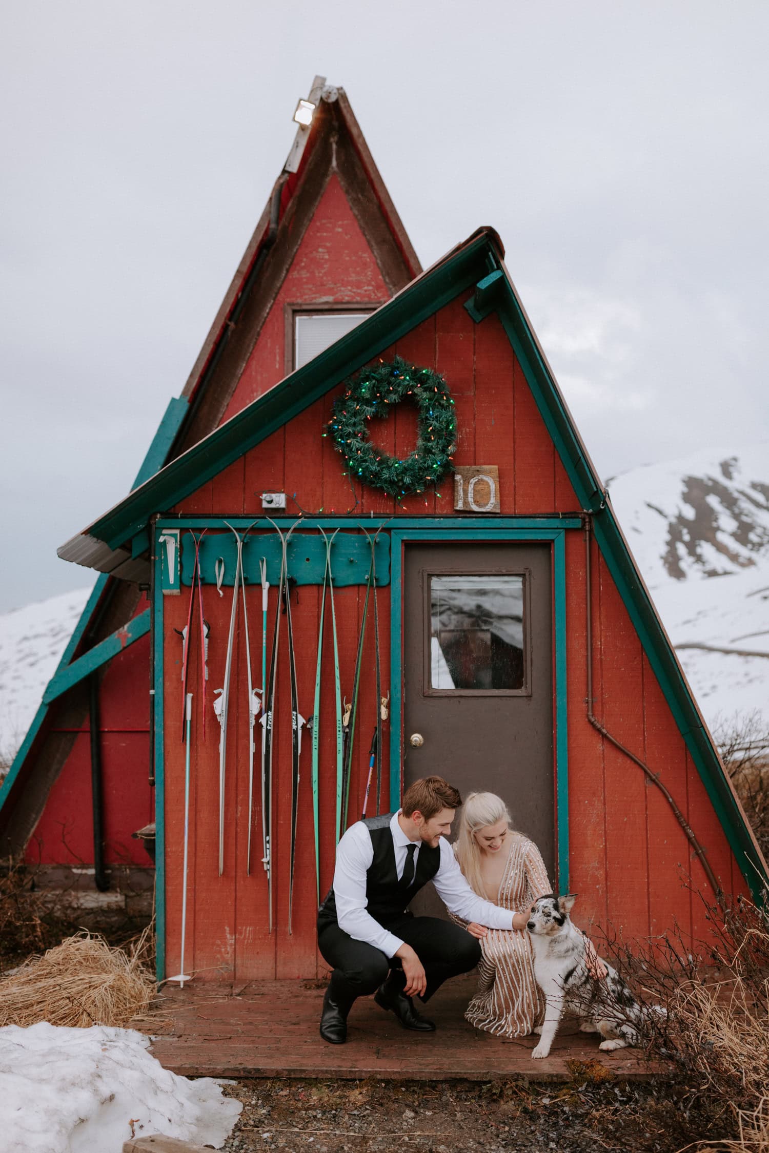 A couple leans down to pet their dog during their snowy Hatcher Pass elopement in Alaska.