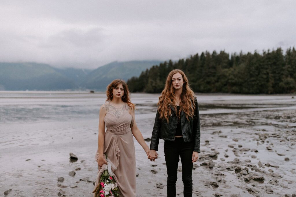 A couple holds hands standing side by side on the beach in Resurrection Bay for their Seward, Alaska elopement.