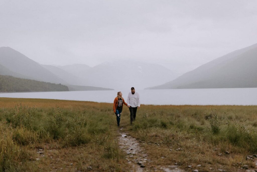 A couple walks while holding hands by  Eklunta Lake with scenic mountain views, known for being one of the best places to elope in Alaska.