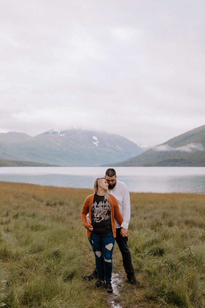 A couple poses in an embrace in front of one of the best places to elope in Alaska: Eklunta Lake.