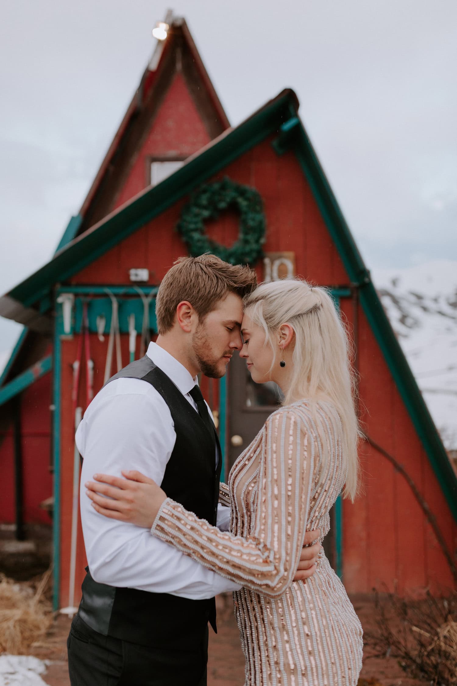 A couple presses foreheads and embraces in front of a red cabin at Hatcher Pass Lodge in Alaska.