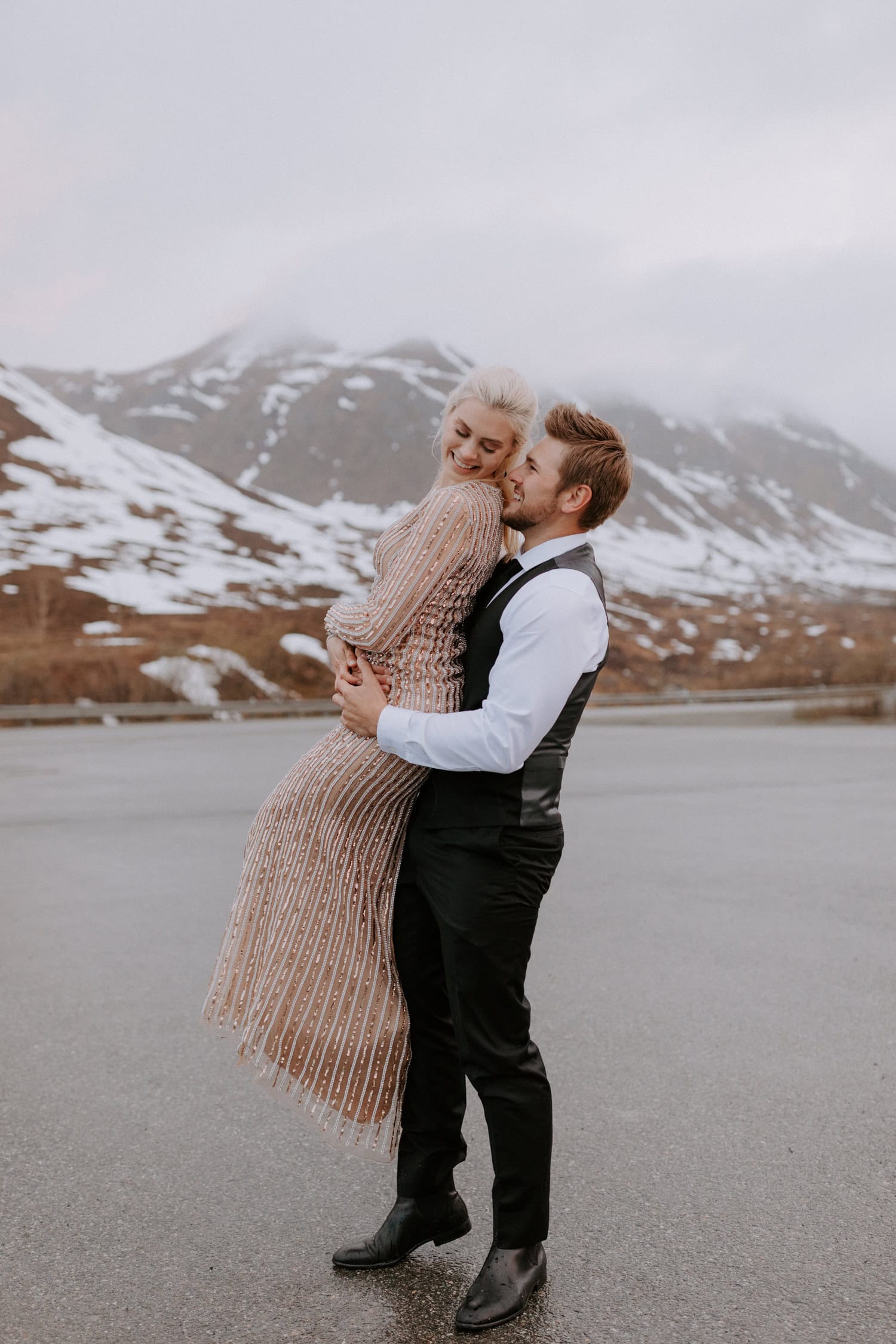 A groom picks up his bride and spins her around for fun during their snowy mountaintop elopement at Hatcher Pass, Alaska.