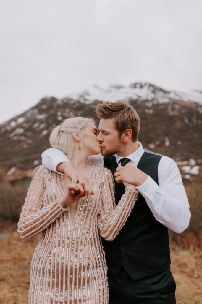 A couple kisses in front of a snow-capped mountain during their Alaska elopement at Hatcher Pass.
