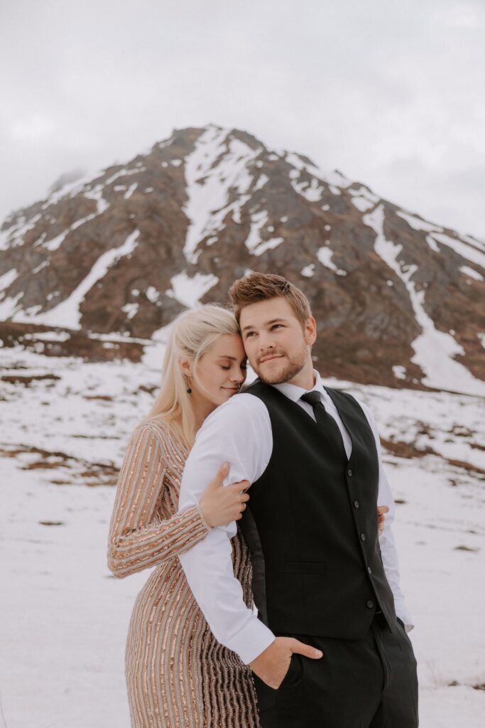 A couple embraces in front of a snow covered mountain peak during their Alaska elopement at Hatcher Pass.