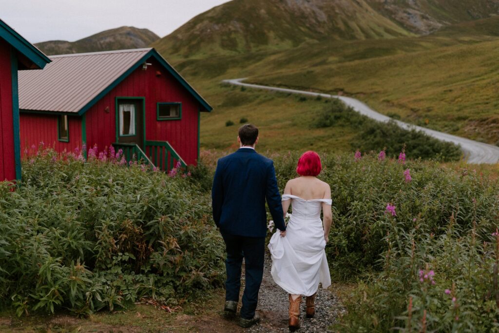 A bride and groom walk past the tiny red cabins at Hatcher Pass.