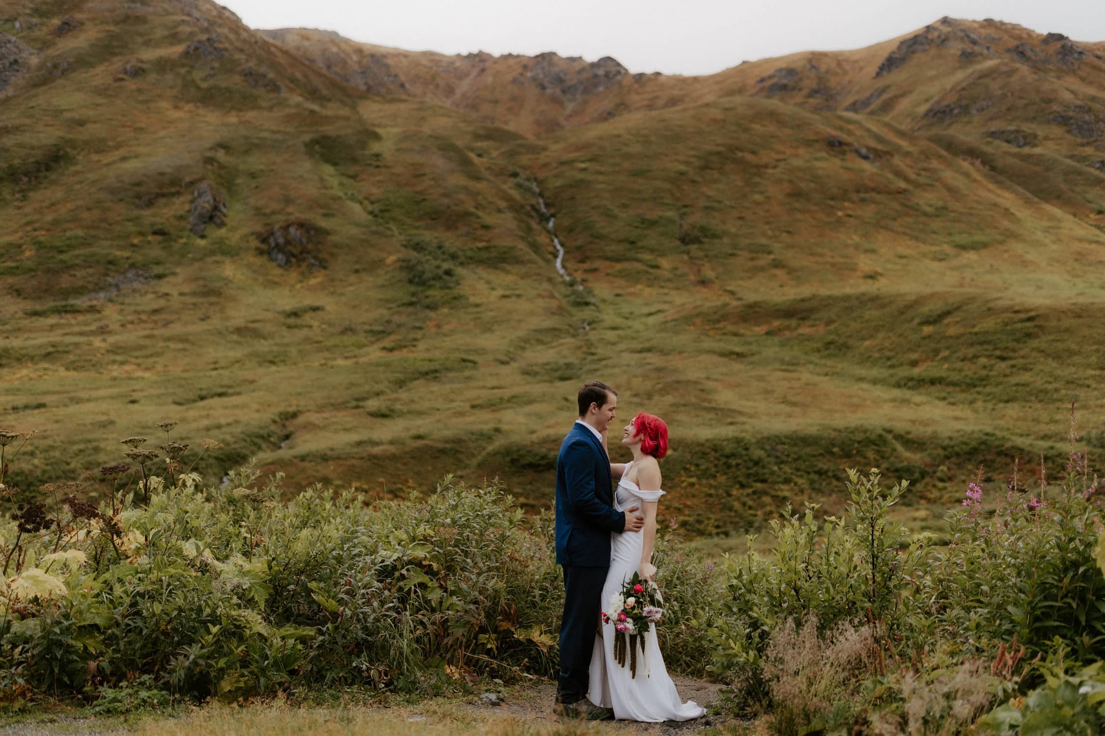 A couple standing in front of a small waterfall at Hatcher Pass Lodge for their elopement.