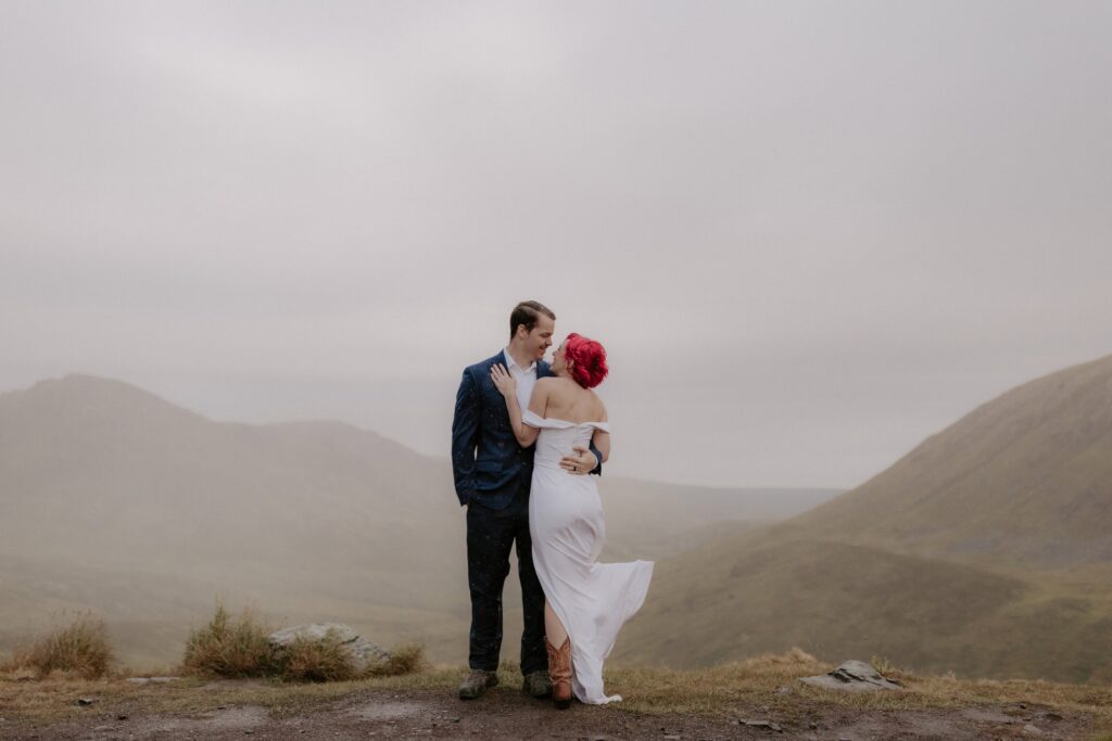 A couple embraces in front of a rain-soaked Hatcher Pass Valley during their Alaska adventure elopement.