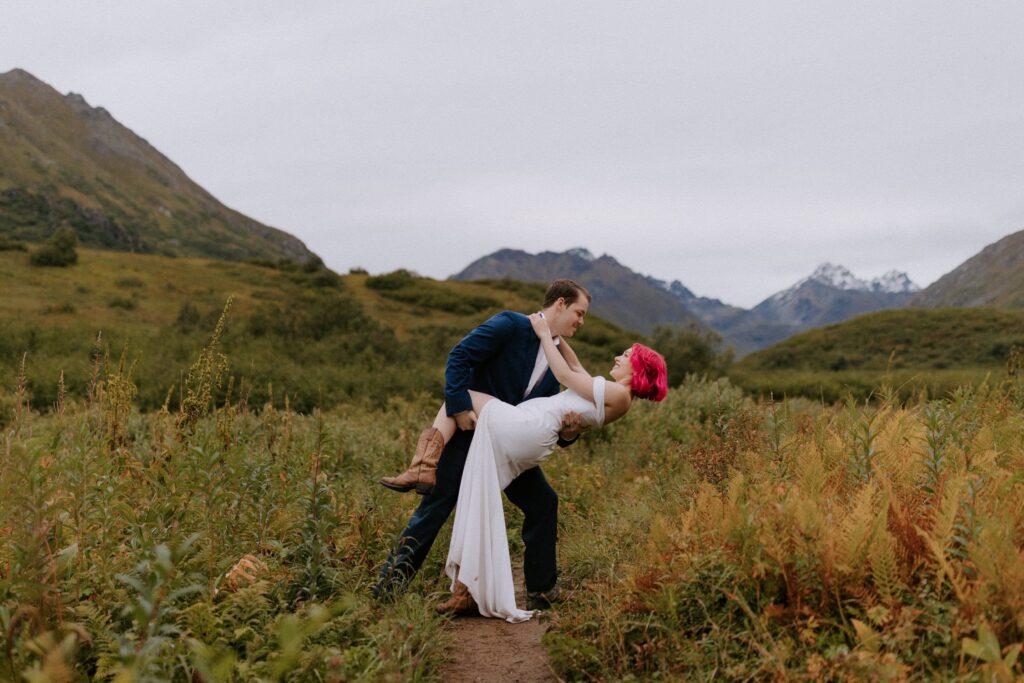 A groom dips his bride down for a kiss on the Gold Mint Trail at Hatcher Pass, Alaska.