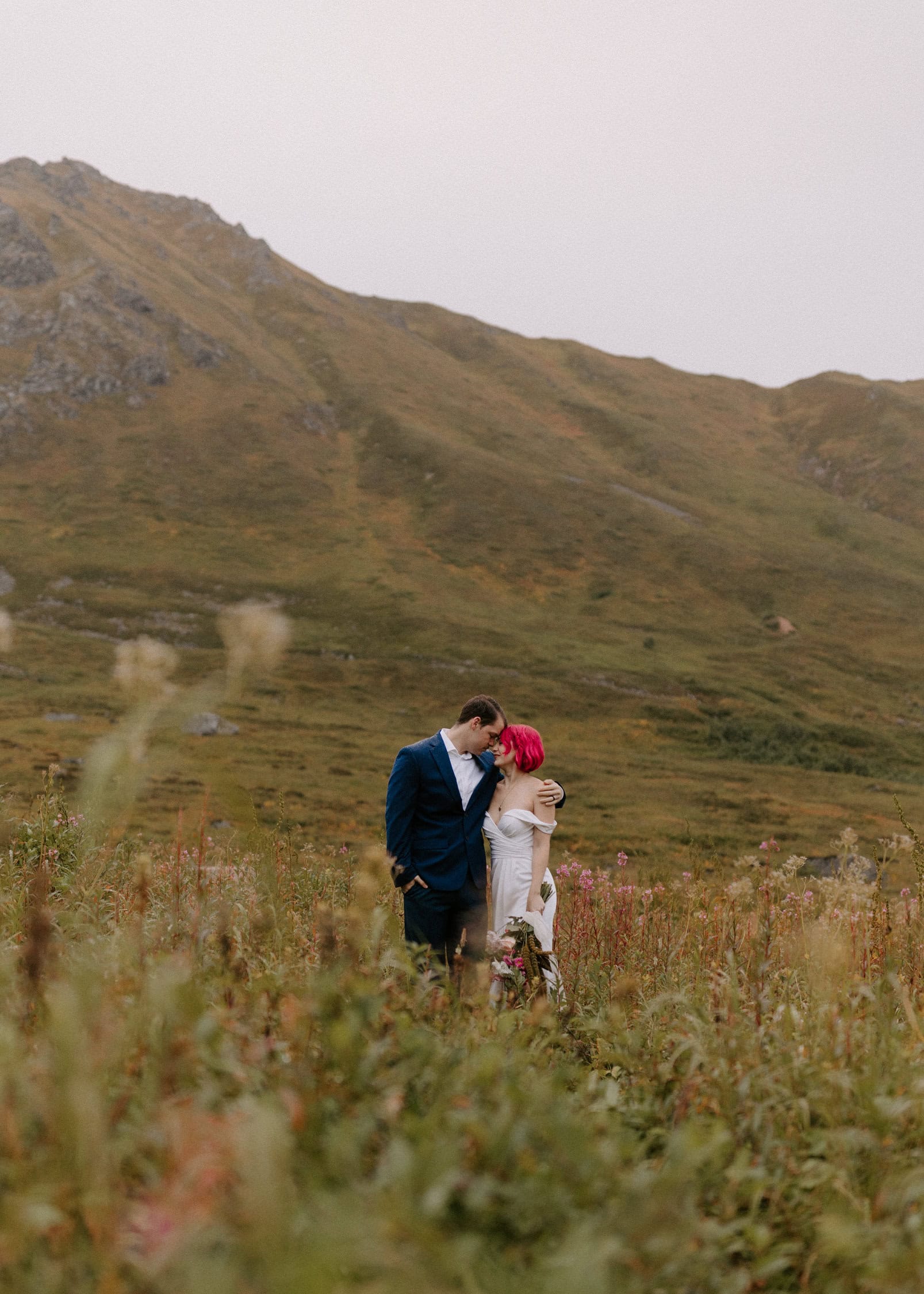 A bride and groom in wedding attire embrace in the mountains of Hatcher Pass.