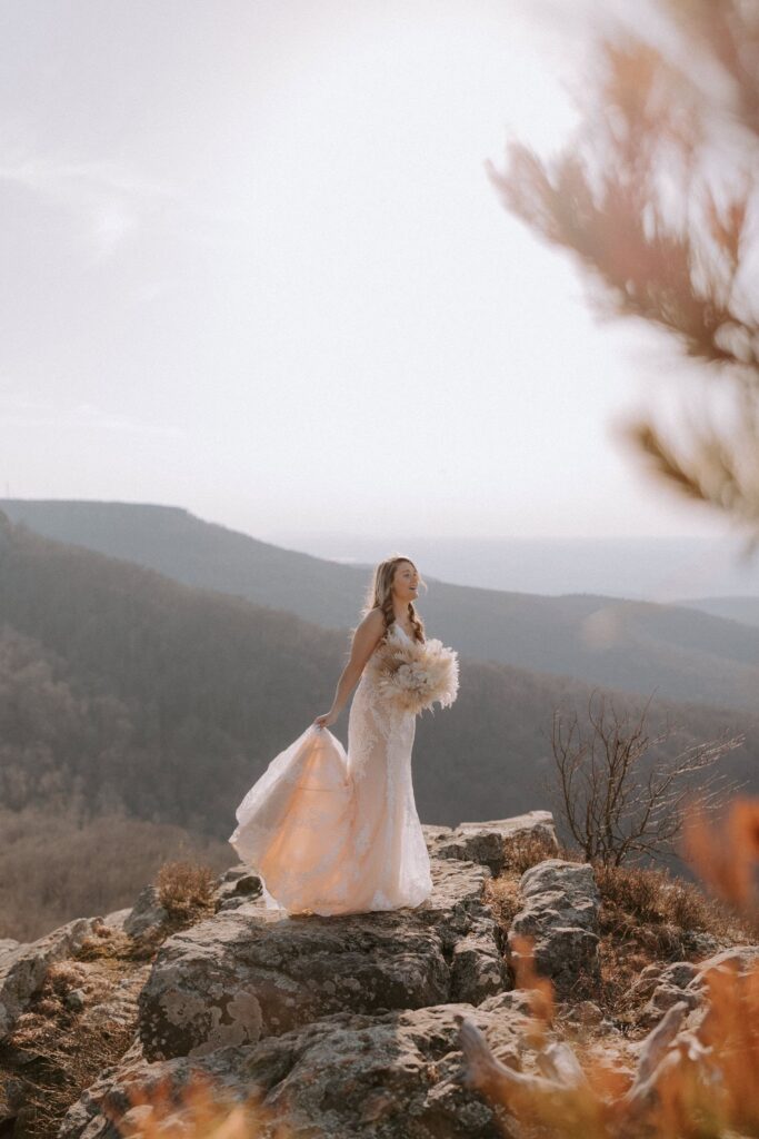 A bride picks up her dress and poses for a photo on a cliffside at Cameron Bluff on Mount Magazine in Arkansas.