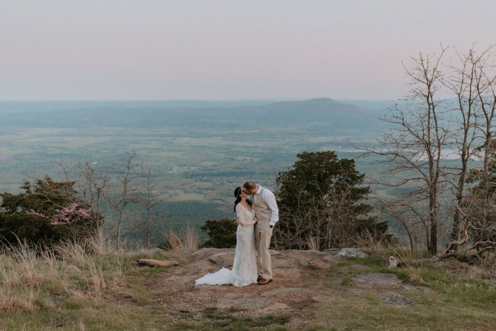 A couple in wedding attire kisses on an overlook behind Mount Magazine State Park Lodge.