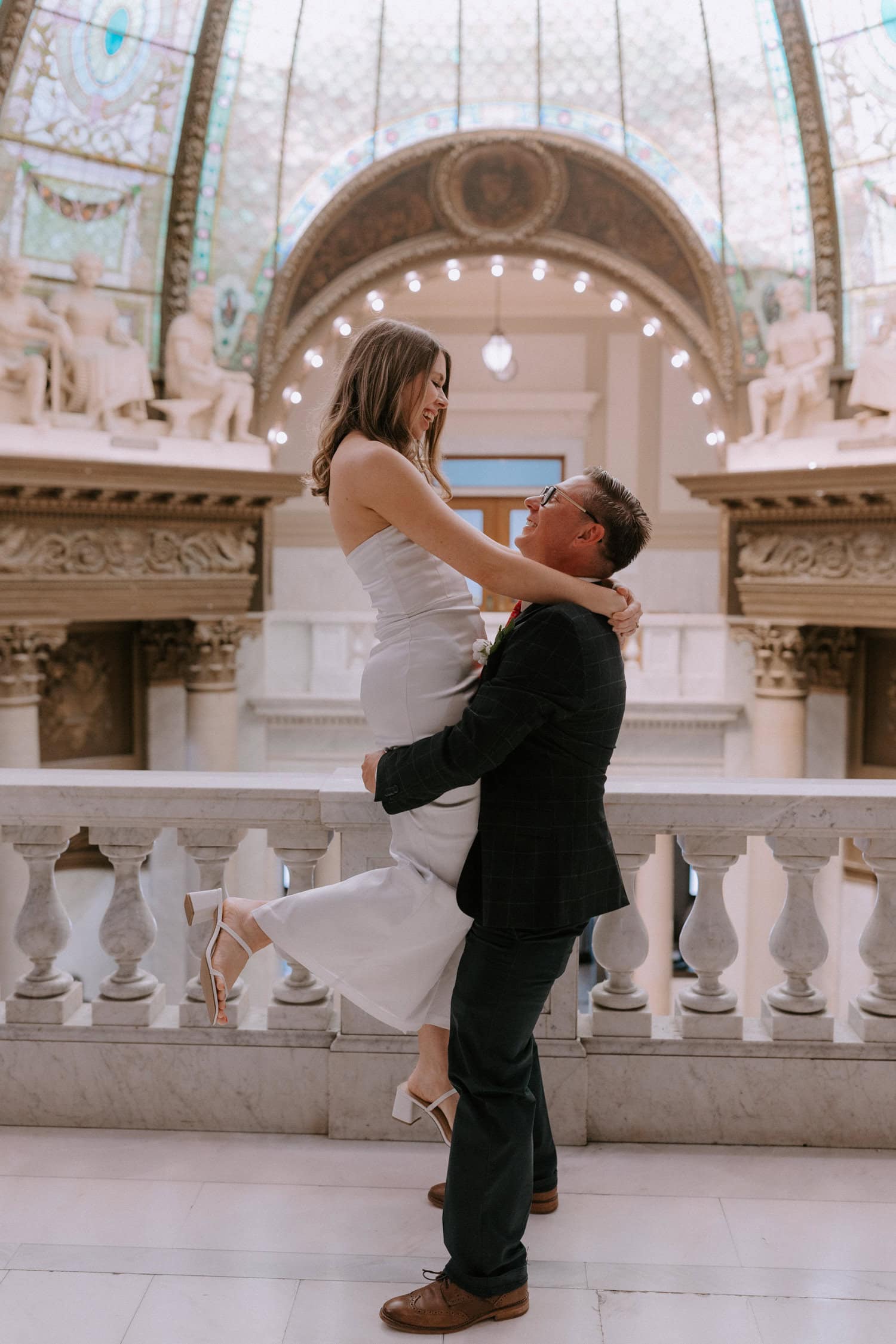 A groom picks up his bride and spins her around during elopement photos at the Pulaski County Courthouse in Little Rock, Arkansas.