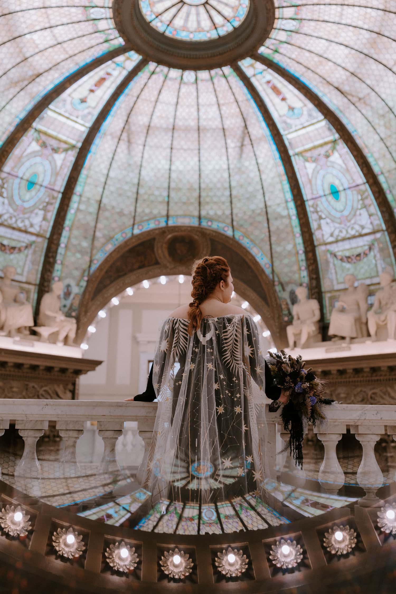 A bride's back is to the camera as she looks out over the balcony to view the stained glass dome at Pulaski County Courthouse in Little Rock, Arkansas.