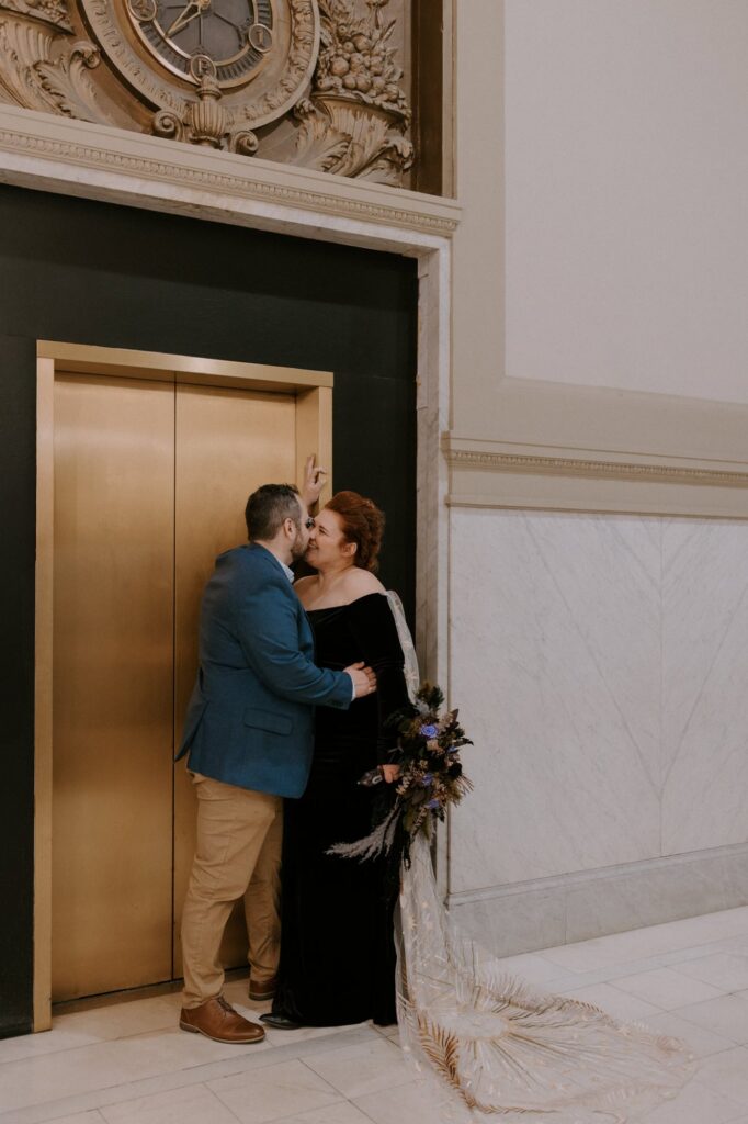 A groom leans in to kiss his bride in front of the golden elevators at Pulaski County Courthouse in Little Rock.
