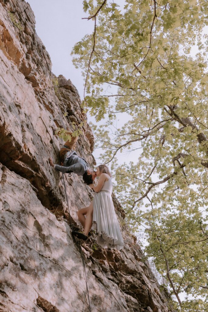 A bride and groom kiss from the side of a cliff while rock climbing at Petit Jean State Park during their vow renewal in Arkansas.