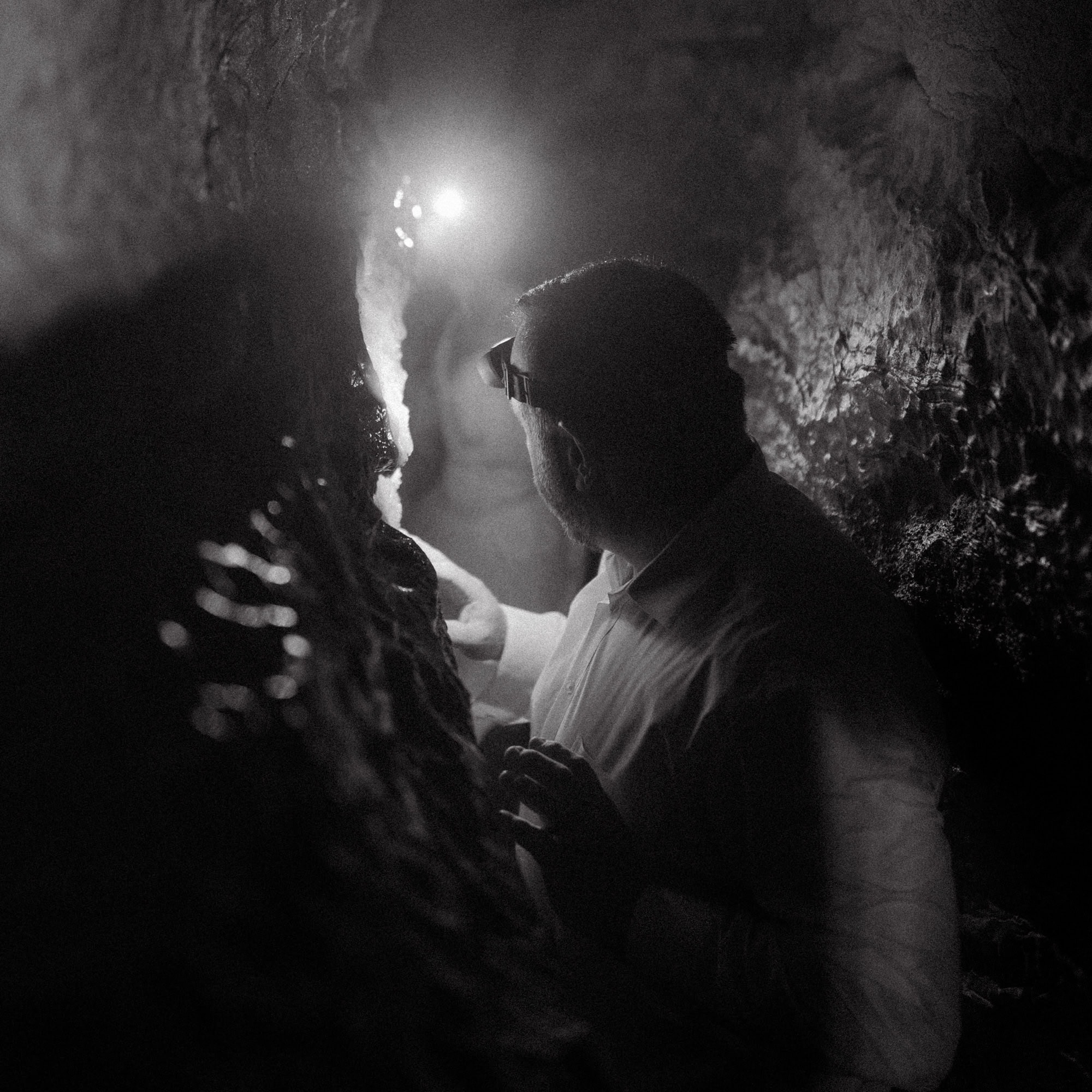 A groom squeezes through a tight corner of Eden Falls Cave while exploring during a Lost Valley Trail Elopement in Ponca, Arkansas.
