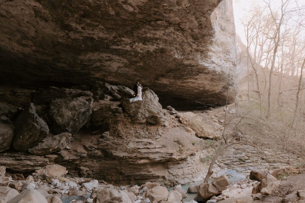 A bride and groom pose for a photo on top of a high rock inside Cob Cave at Lost Valley Trail in Ponca, Arkansas.
