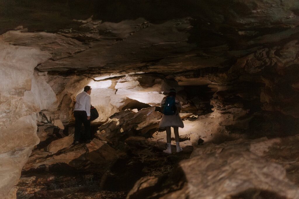 A couple begins to climb into Eden Falls Cave with their flashlights to explore during their adventure elopement at Lost Valley in Ponca, Arkansas.