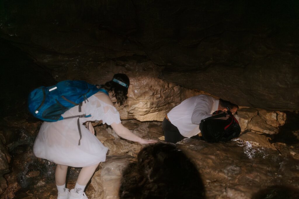A couple drops low to crawl through Eden Falls Cave during their Lost Valley elopement.