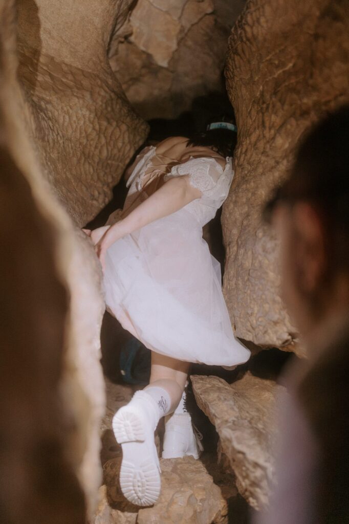 A bride crawls through Eden Falls Cave in her dress during a Lost Valley Trail elopement.
