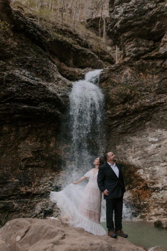 A bride and groom stand below Eden Falls at Lost Valley Trail in Ponca, Arkansas during their adventure vow renewal.