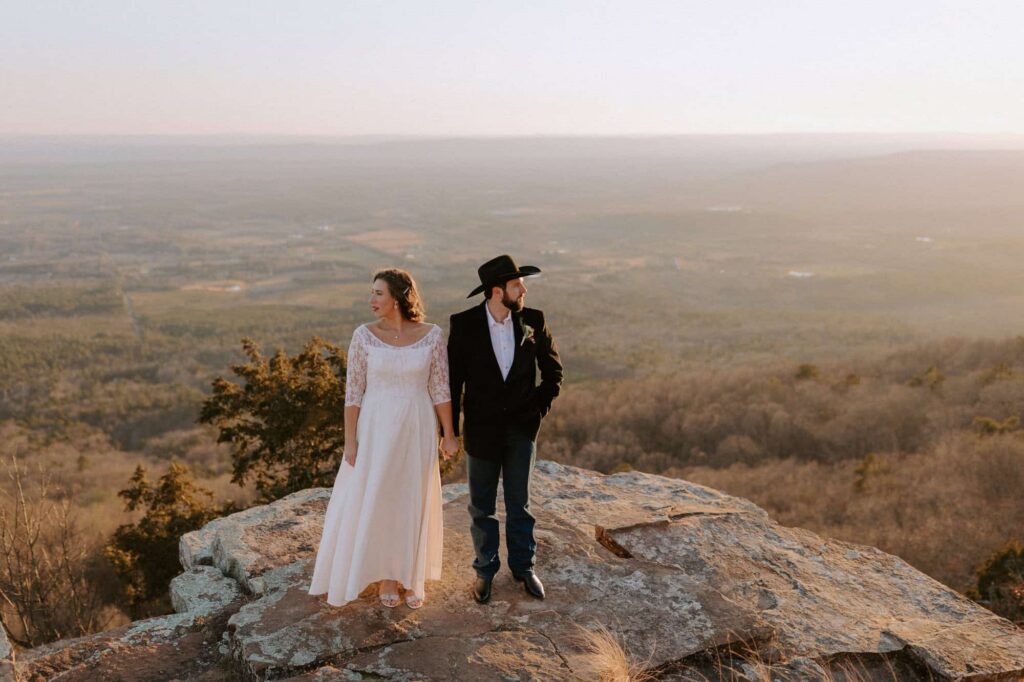 A bride and groom pose for photos on a ledge overlooking the valley at Mt. Nebo during their elopement.