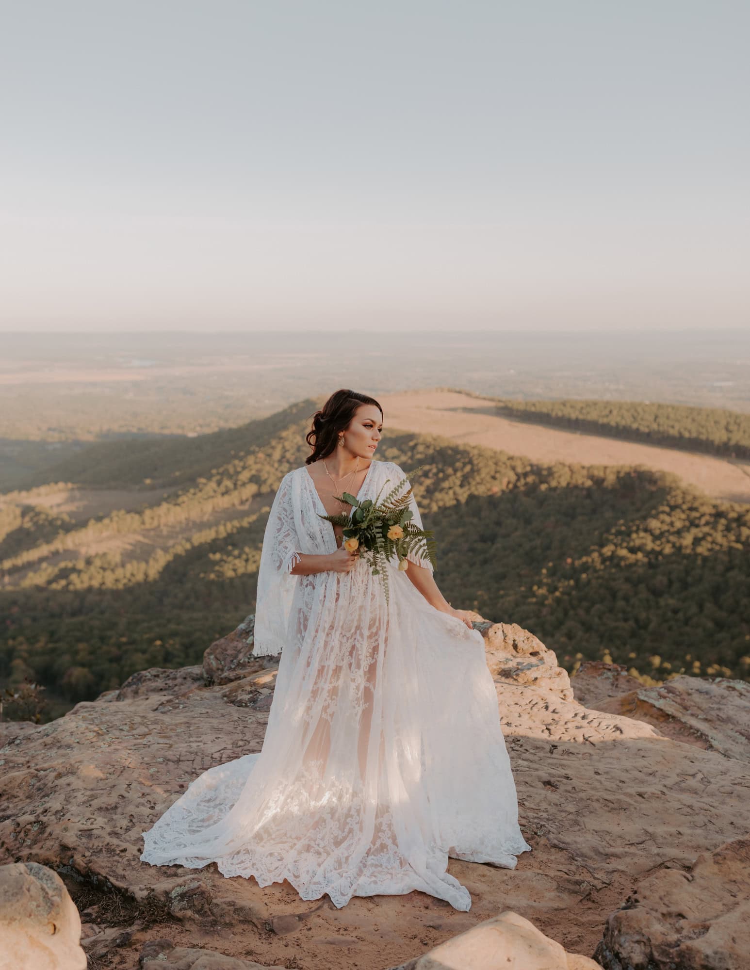 A bride poses for a photo with her bouquet at Sunrise Pt. Overlook on Mt. Nebo State Park.