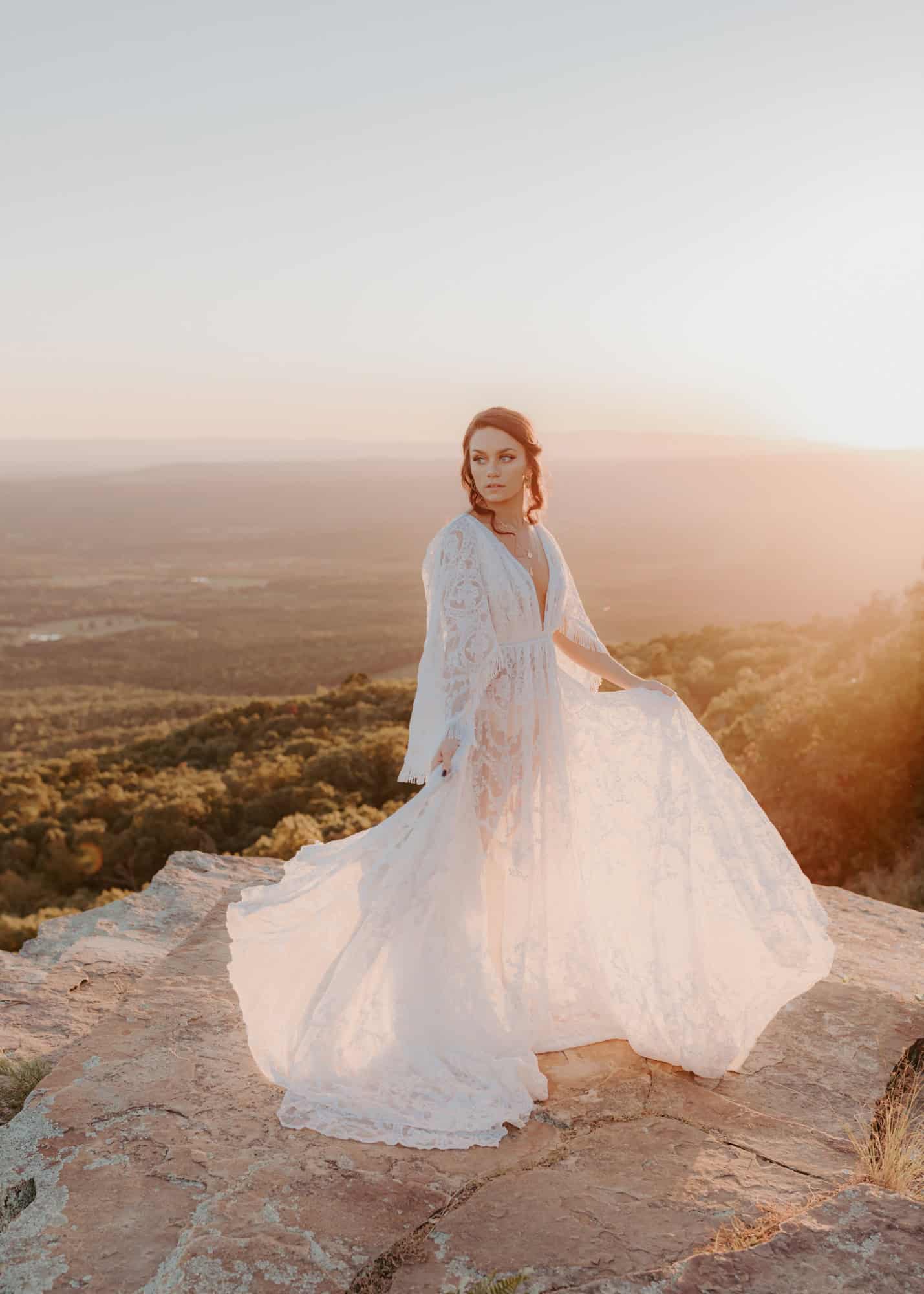 A bride stands on Sunrise Overlook at Mt Nebo in Arkansas during a golden glowing sunset.