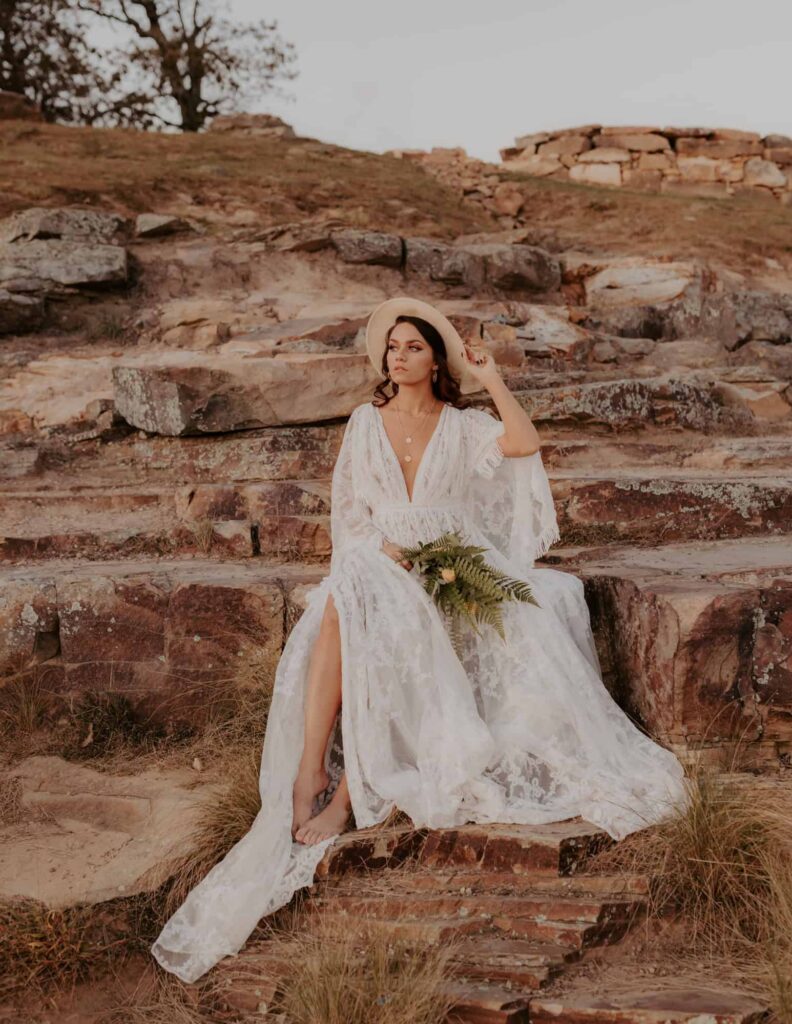 A bride poses for a photo while sitting on a rocky ledge during a Mt. Nebo elopement.