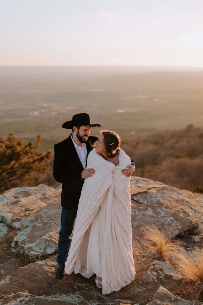 A groom wraps his bride into a blanket on an overlook during their Mt. Nebo wedding.