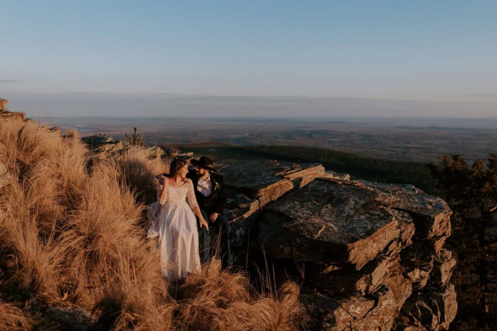 A bride and groom sit on a ledge at an overlook on top of Mt. Nebo State Park during their wedding on the mountain.