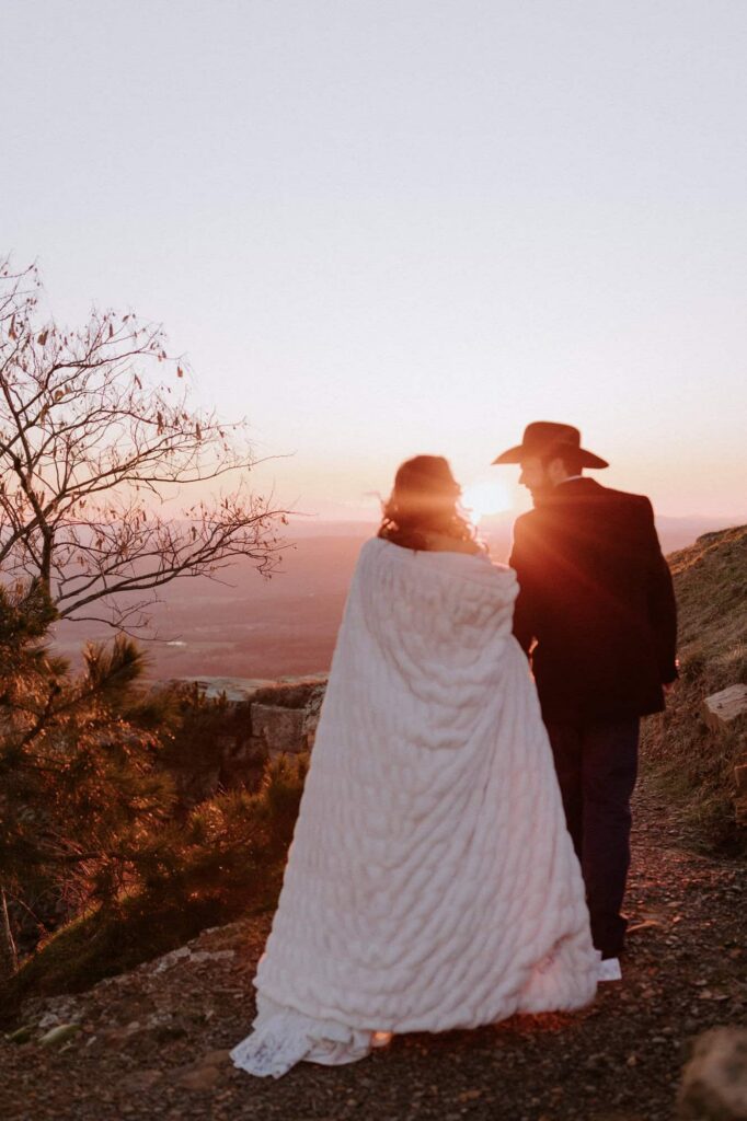 An eloping couple walks towards the sunset along a trail at Sunrise Pt Overlook on Mt. Nebo State Park.
